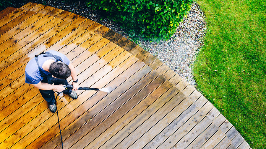 a man is cleaning a wooden deck with a pressure washer